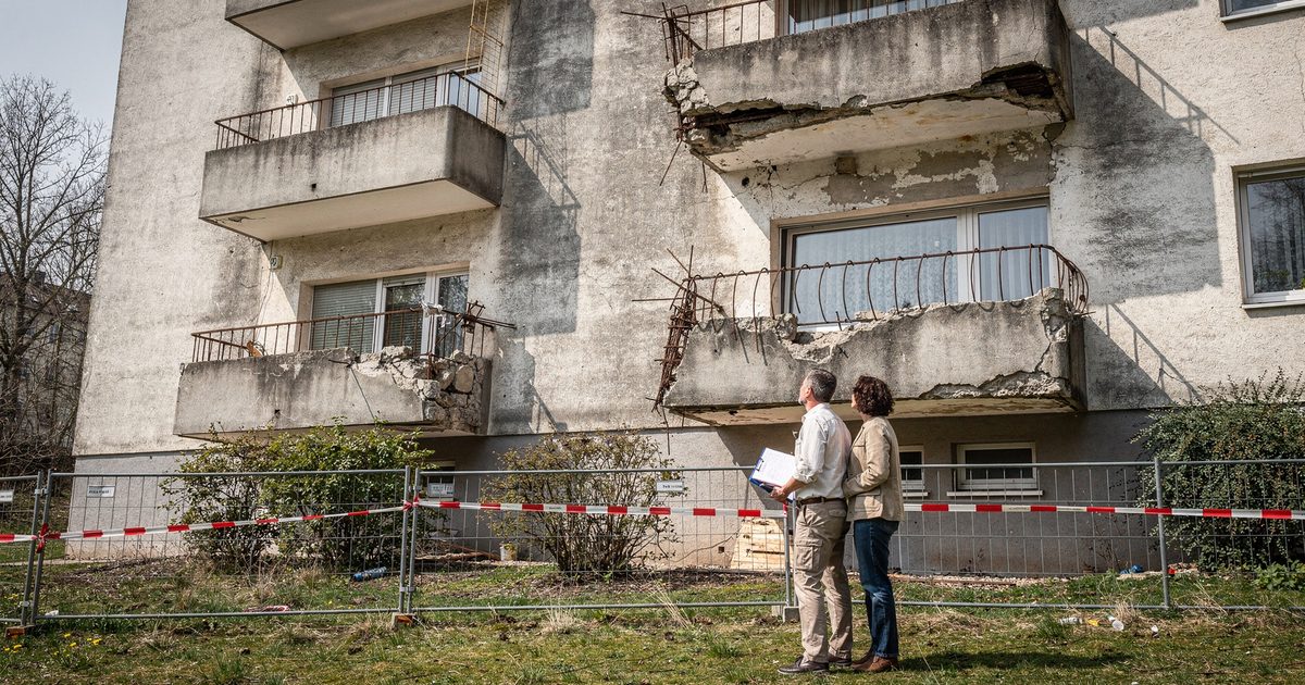 Mehrere sanierungsbedürftige Betonbalkone an einem Mehrfamilienhaus, darunter eine mit Bauzaun abgesperrte Grünfläche