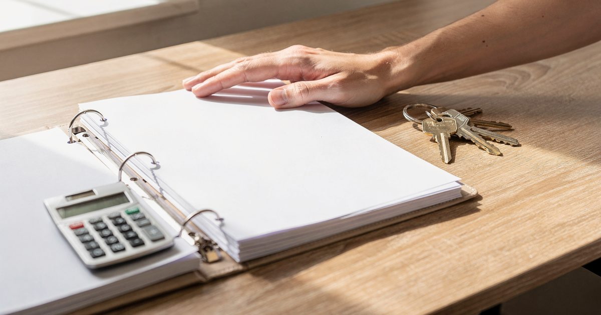Schreibtisch mit aufgeschlagenem Ordner, Papierunterlagen, Taschenrechner und einem Schlüsselbund im Tageslicht